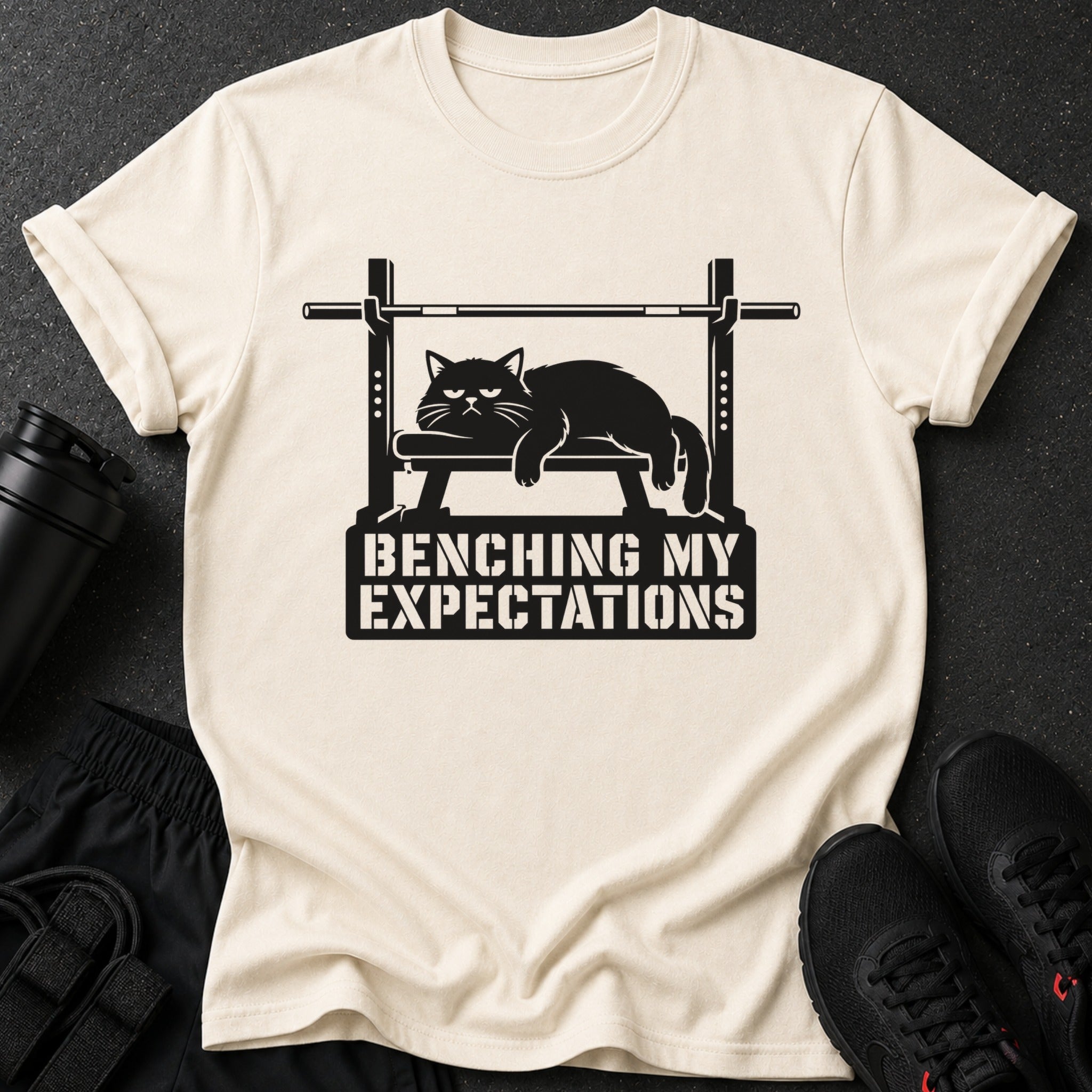 T-shirt with black cat on weight bench graphic and text "BENCHING MY EXPECTATIONS".