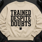 Tan sweatshirt with black distressed text "TRAINED DESPITE DOUBTS" and a kettlebell graphic.