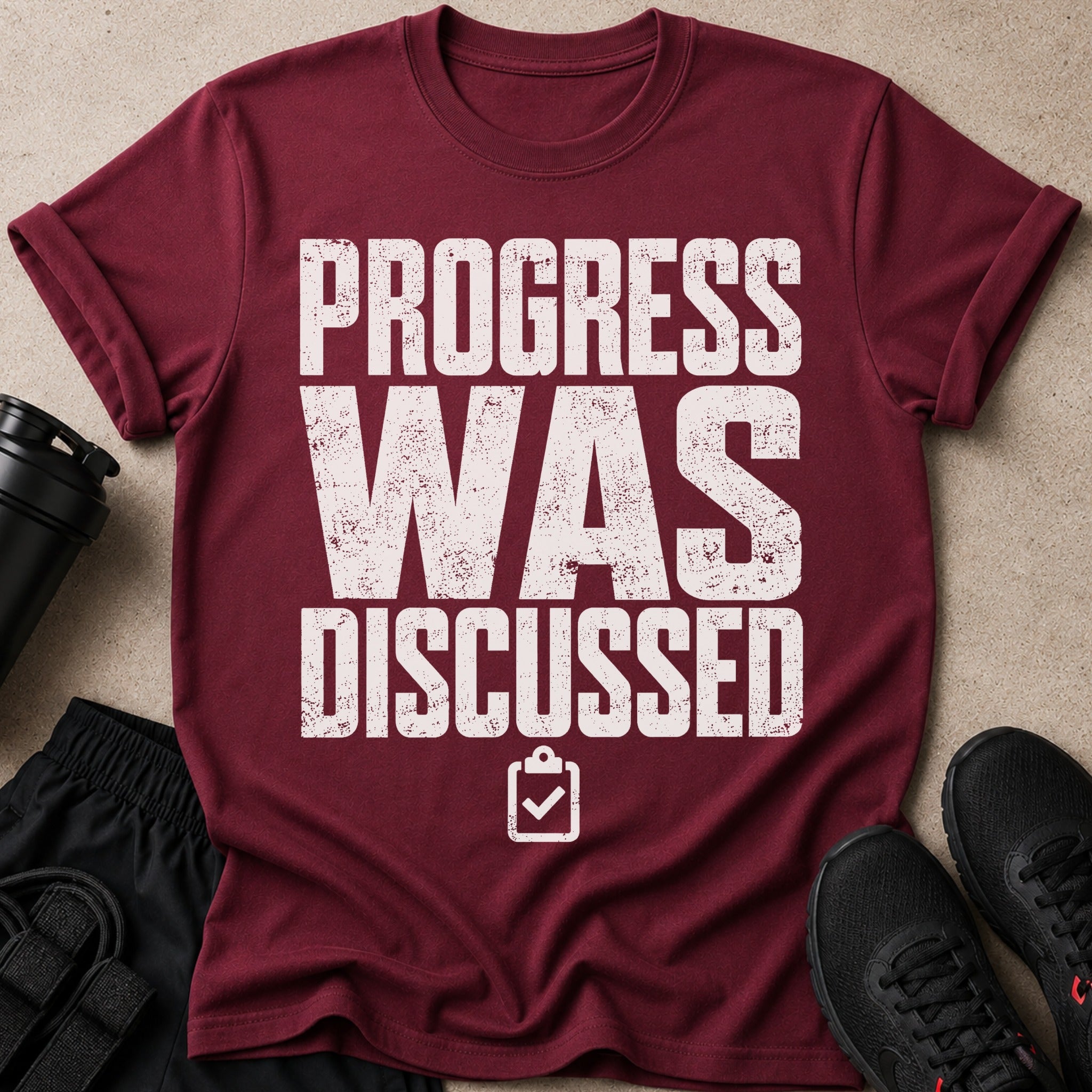 Maroon t-shirt with white text "PROGRESS WAS DISCUSSED" and a clipboard icon.