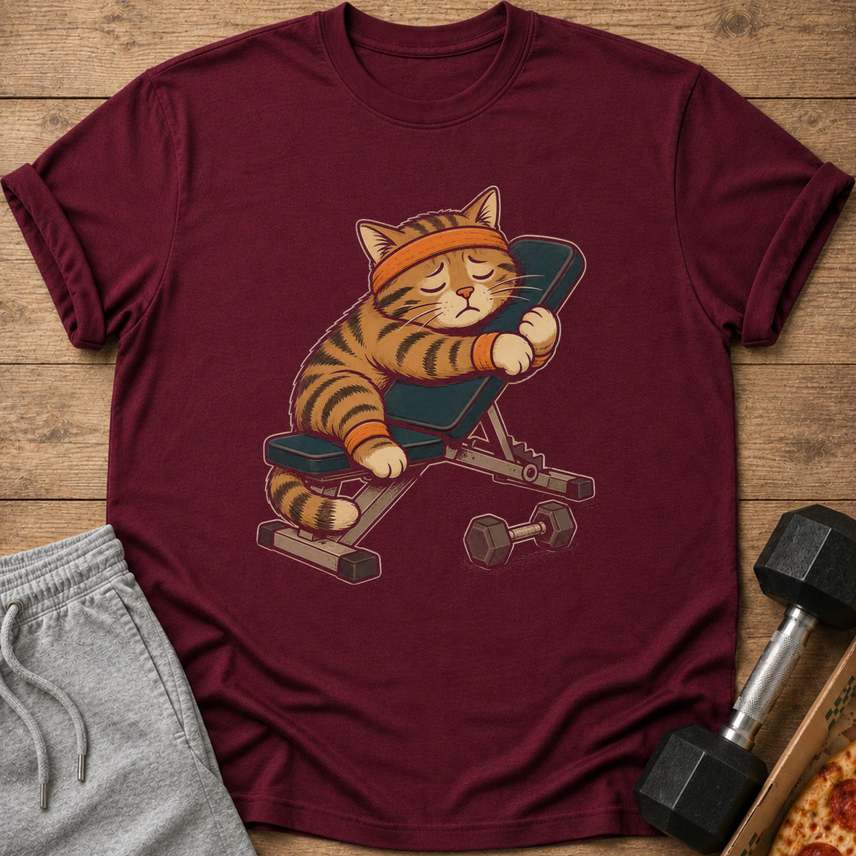 Maroon t-shirt with a cartoon cat sleeping on a weight bench.