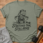 Opossum struggling with resistance bands, text reads "Stretched Thin, Still Here."