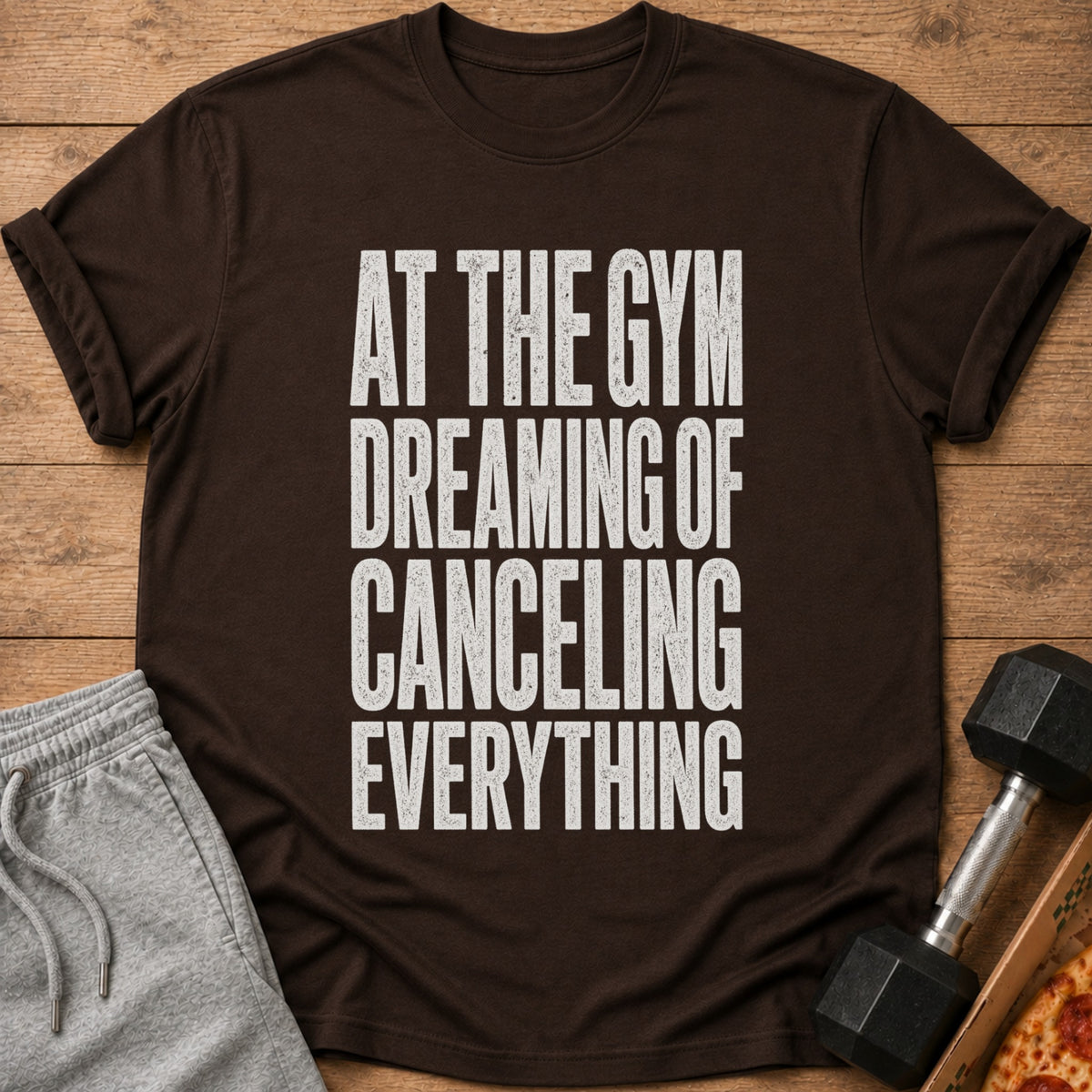 Brown t-shirt with white text that reads "AT THE GYM DREAMING OF CANCELING EVERYTHING."