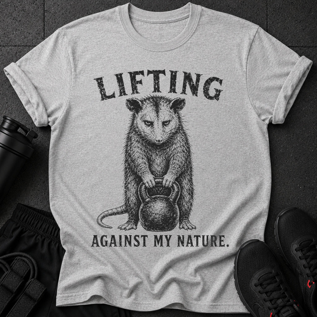Grey t-shirt with possum holding kettlebell and text "LIFTING AGAINST MY NATURE."