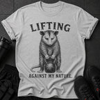 Grey t-shirt with possum holding kettlebell and text "LIFTING AGAINST MY NATURE."