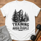Bigfoot lifting weights with text "TRAINING TO AVOID PEOPLE" on a white shirt.