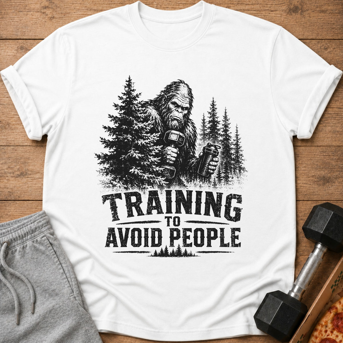 Bigfoot lifting weights with text "TRAINING TO AVOID PEOPLE" on a white shirt.
