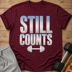Maroon t-shirt with white and blue text "STILL COUNTS" and barbell graphic.