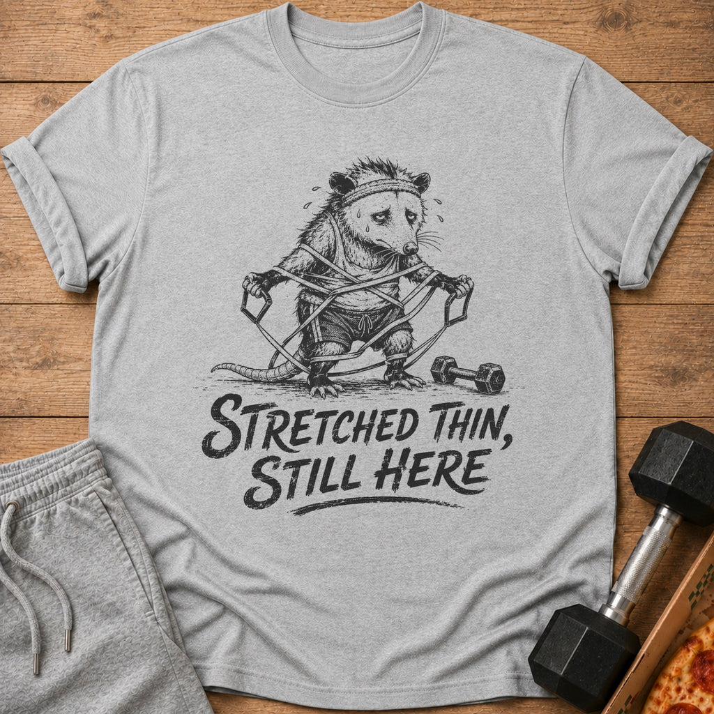 Grey t-shirt with a sketch of a tired possum working out, text reads "Stretched Thin, Still Here".