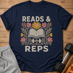 Navy blue t-shirt featuring floral illustrations, an open book, a dumbbell, and the text READS & REPS.