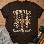 Brown t-shirt with "PENCILS & PERSONAL BESTS" text and three decorated pencils.