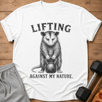 White t-shirt with possum lifting kettlebell and text "Lifting Against My Nature."