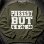 Olive green sweatshirt with white distressed text reading "PRESENT BUT UNINSPIRED".