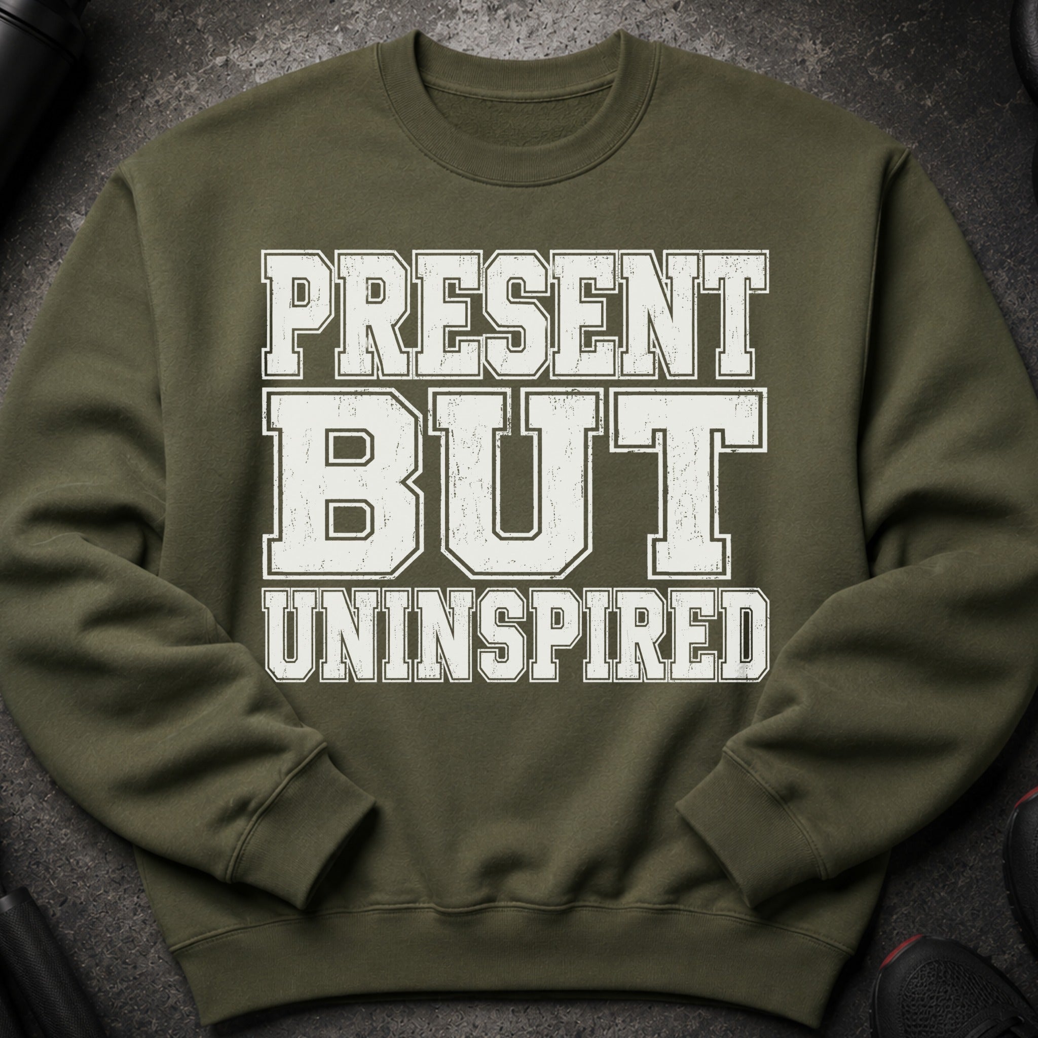 Olive green sweatshirt with white distressed text reading "PRESENT BUT UNINSPIRED".