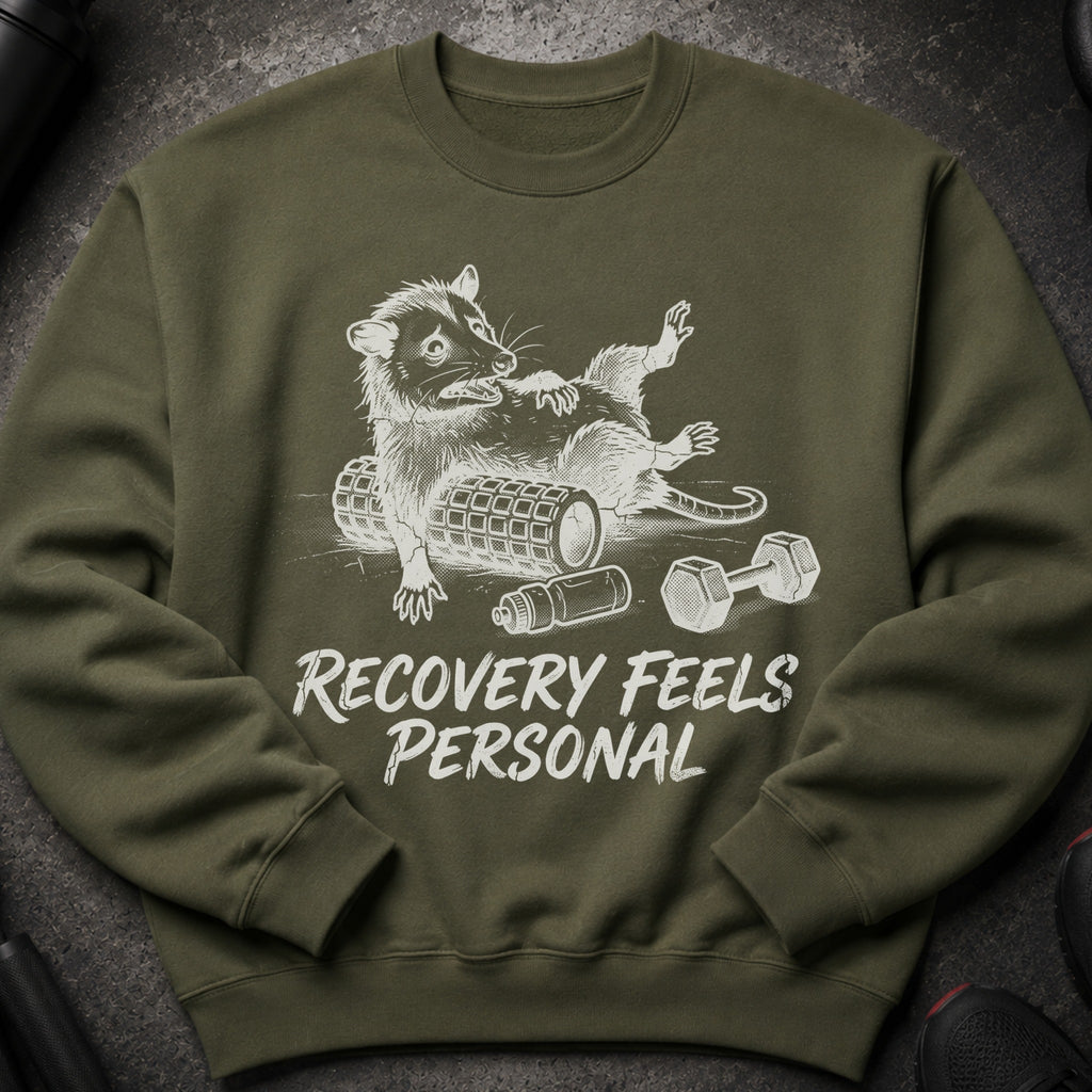 Olive green sweatshirt with a graphic of a possum on a foam roller and dumbbells. Text reads: "RECOVERY FEELS PERSONAL".