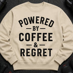Cream sweatshirt with black text reading "POWERED BY COFFEE & REGRET".