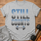 Grey t-shirt with faded blue and grey text "STILL COUNTS" and dumbbell graphic.