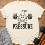 T-shirt graphic of a pear character lifting weights with the word "PRESSURE" below.