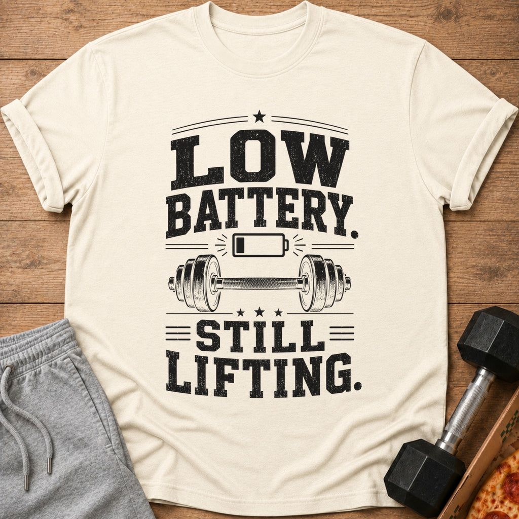 Cream t-shirt with "LOW BATTERY. STILL LIFTING." text, barbell, and battery icon.