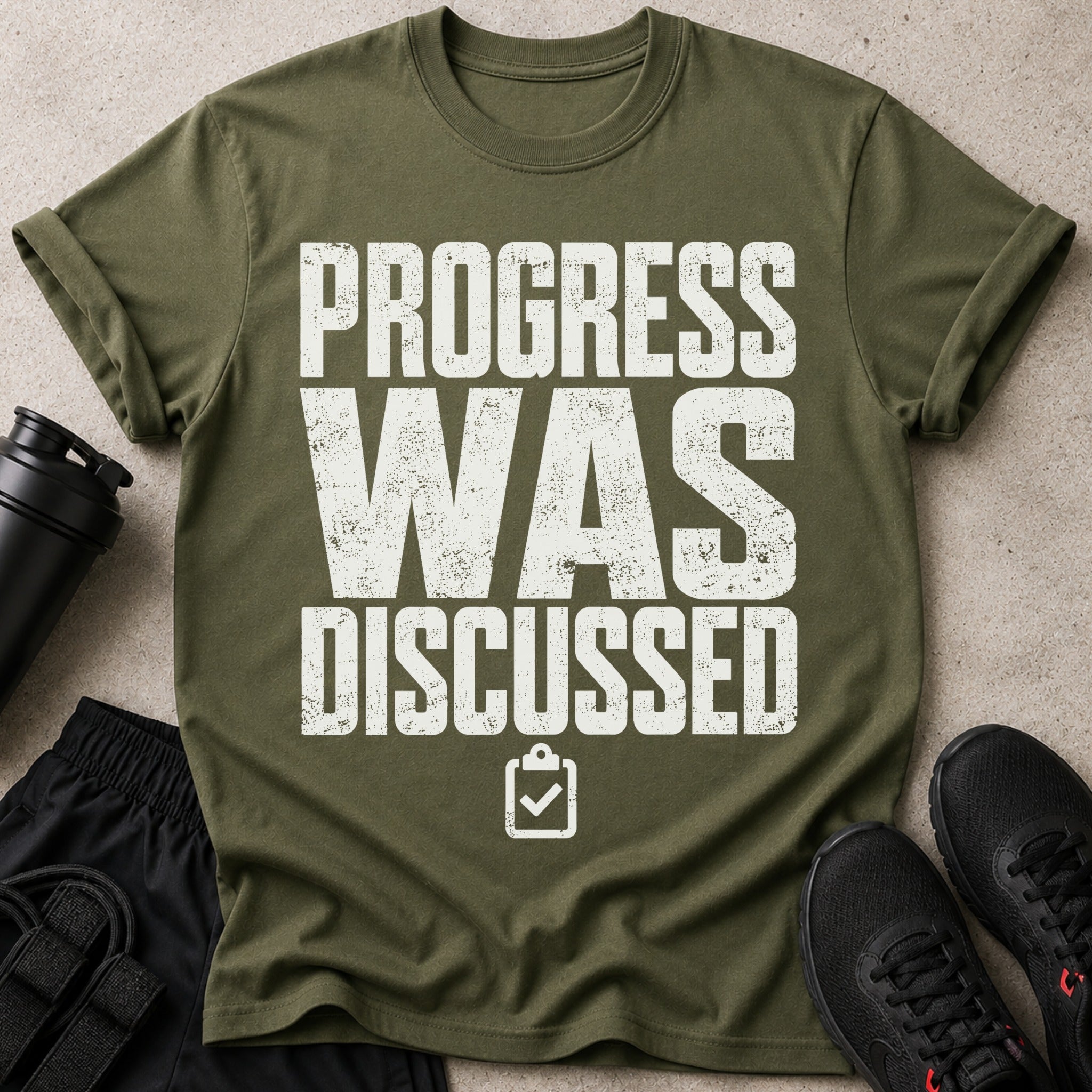 Green t-shirt with white distressed text "PROGRESS WAS DISCUSSED" and a clipboard icon.