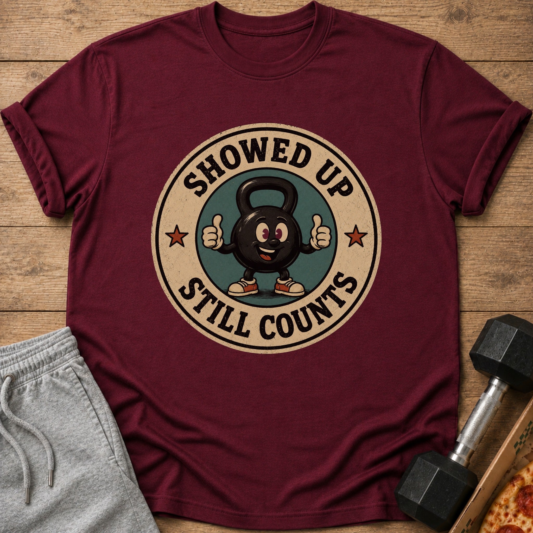 Maroon t-shirt with cartoon kettlebell saying "Showed Up Still Counts".