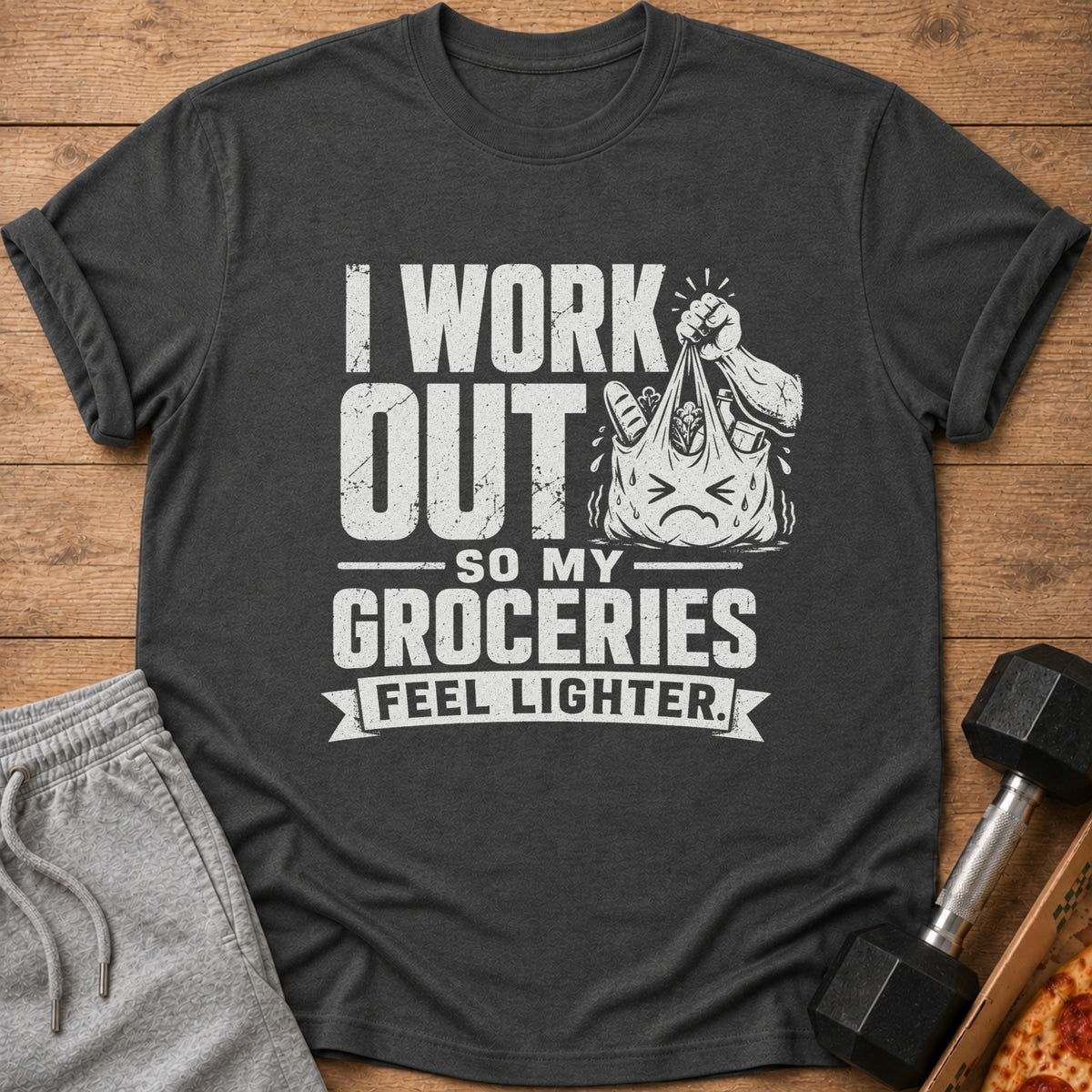 Dark gray t-shirt with white text "I work out so my groceries feel lighter" and cartoon grocery bag.