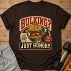 Brown t-shirt with cartoon burger lifting dumbbell, text "BULKING? JUST HUNGRY."