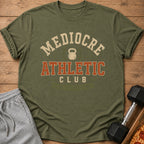 Olive t-shirt with "Mediocre Athletic Club" and kettlebell graphic.
