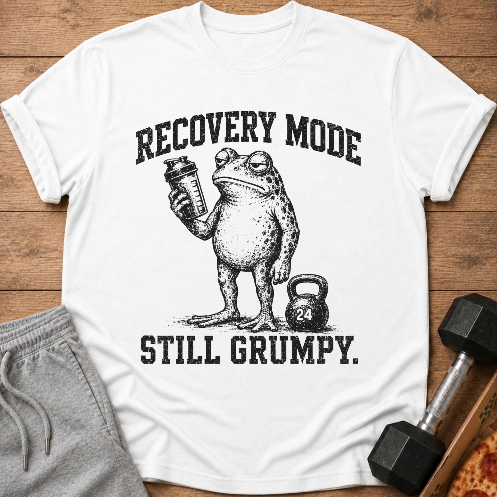 White t-shirt with a grumpy frog holding a shaker bottle and the text "RECOVERY MODE STILL GRUMPY."