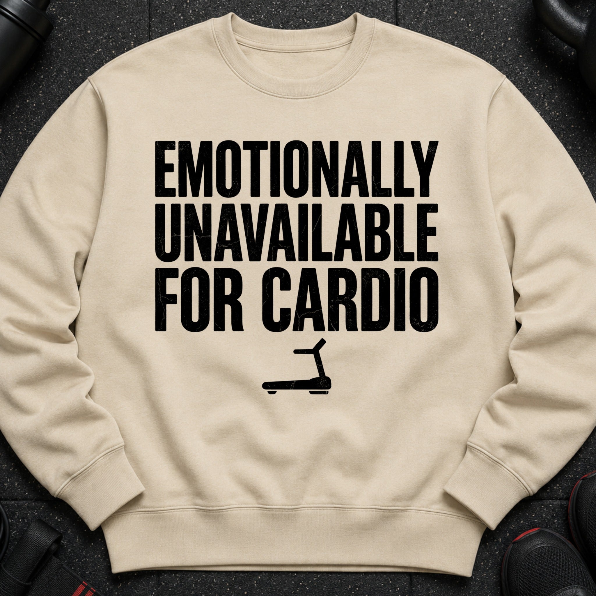 Light beige crewneck sweatshirt with black text reading "EMOTIONALLY UNAVAILABLE FOR CARDIO" and a treadmill graphic.