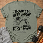 Green t-shirt with illustration of exhausted person, text "TRAINED HARD ENOUGH TO SIT DOWN".