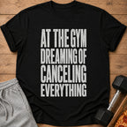 Black t-shirt with white text reading "AT THE GYM DREAMING OF CANCELING EVERYTHING".