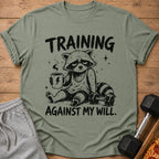 Green t-shirt with a raccoon holding a coffee mug and text "TRAINING AGAINST MY WILL."