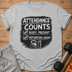 Grey t-shirt with "Attendance Counts" text, body present, motivation absent, and gym icons.