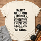 Cream t-shirt with text "I'M NOT GETTING STRONGER, I'M JUST DEVELOPING TRUST ISSUES WITH STAIRS."