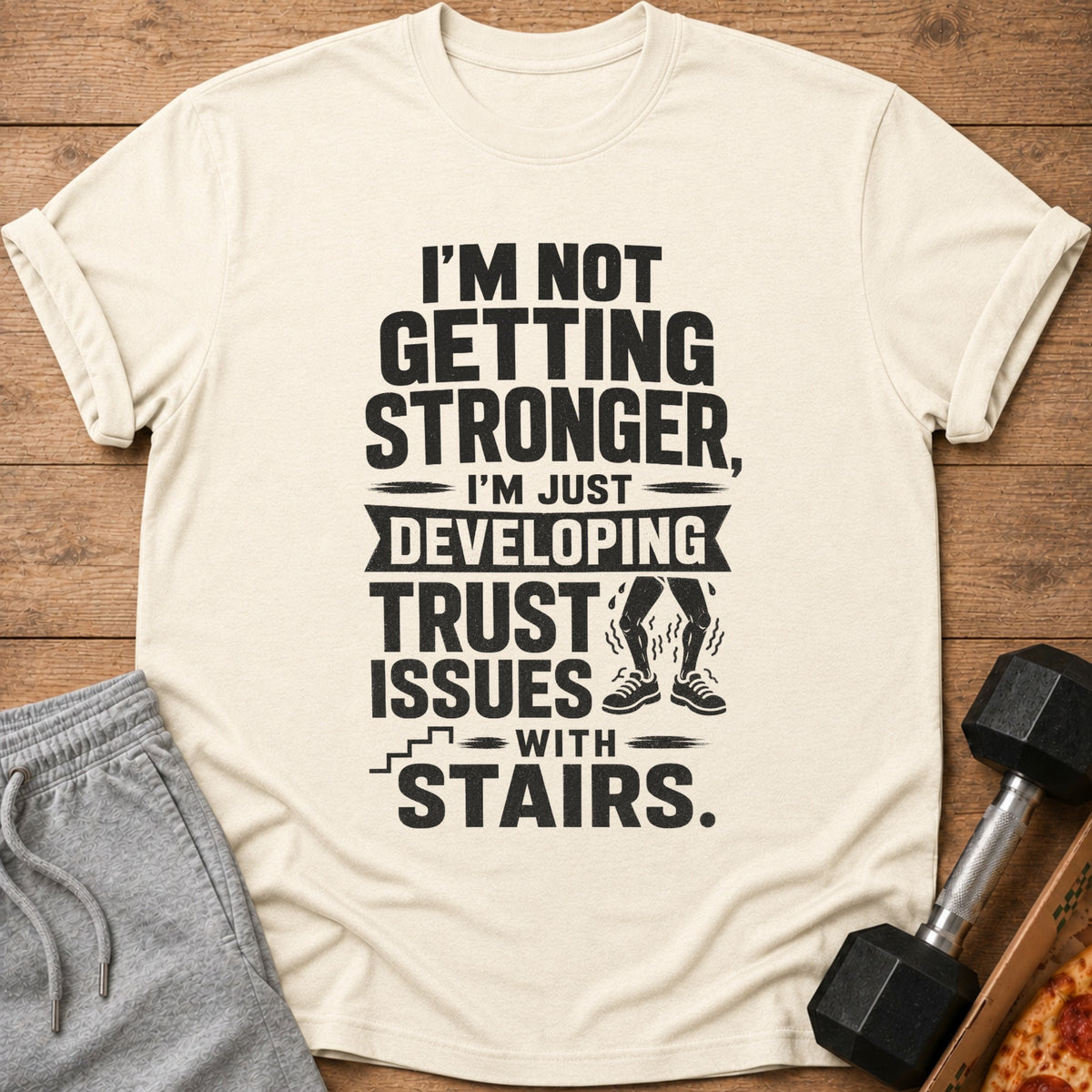 Cream t-shirt with text "I'M NOT GETTING STRONGER, I'M JUST DEVELOPING TRUST ISSUES WITH STAIRS."