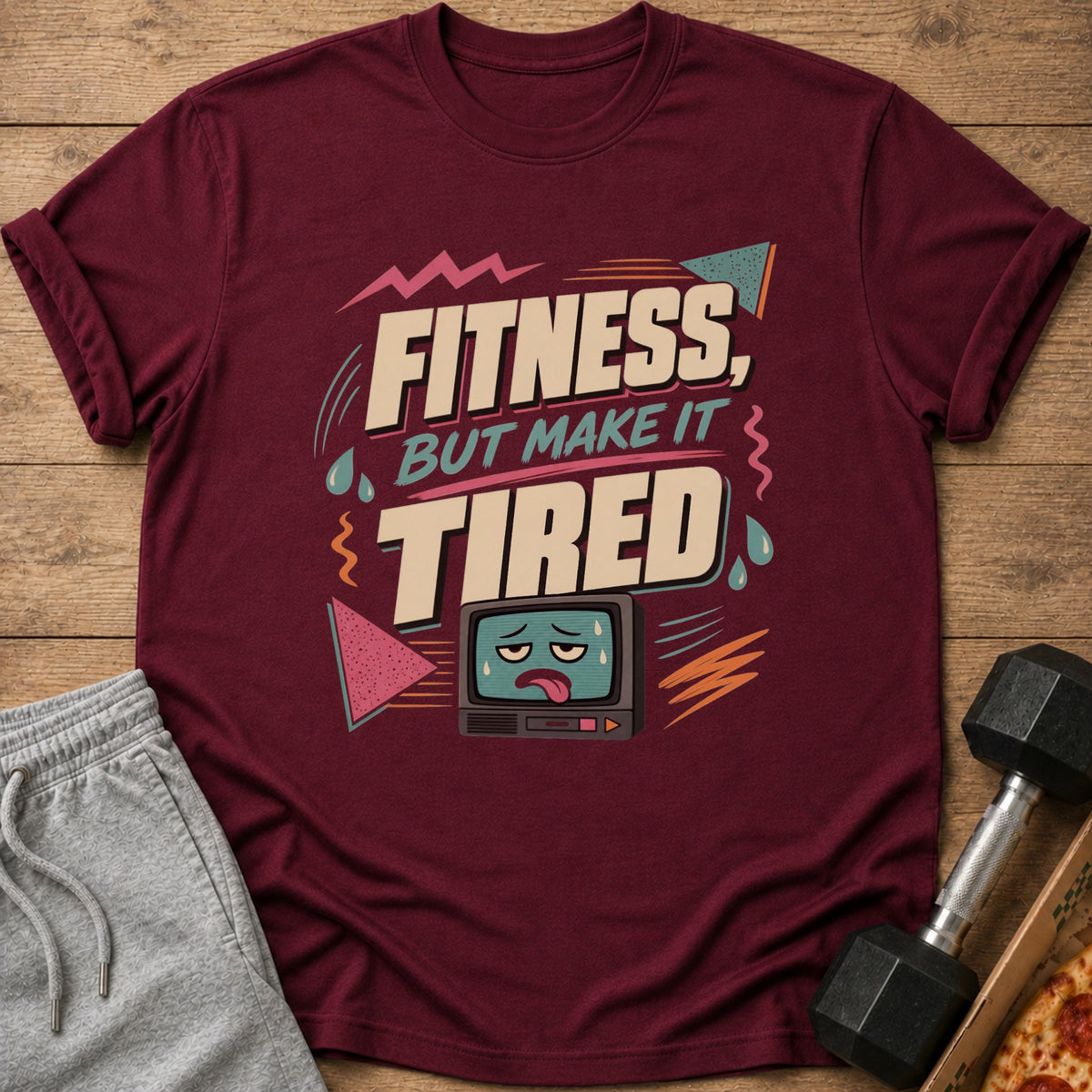 Maroon t-shirt with text "Fitness, But Make It Tired" and a tired television graphic.