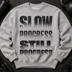 Grey sweatshirt with "SLOW PROGRESS STILL PROGRESS" printed on the front in black.