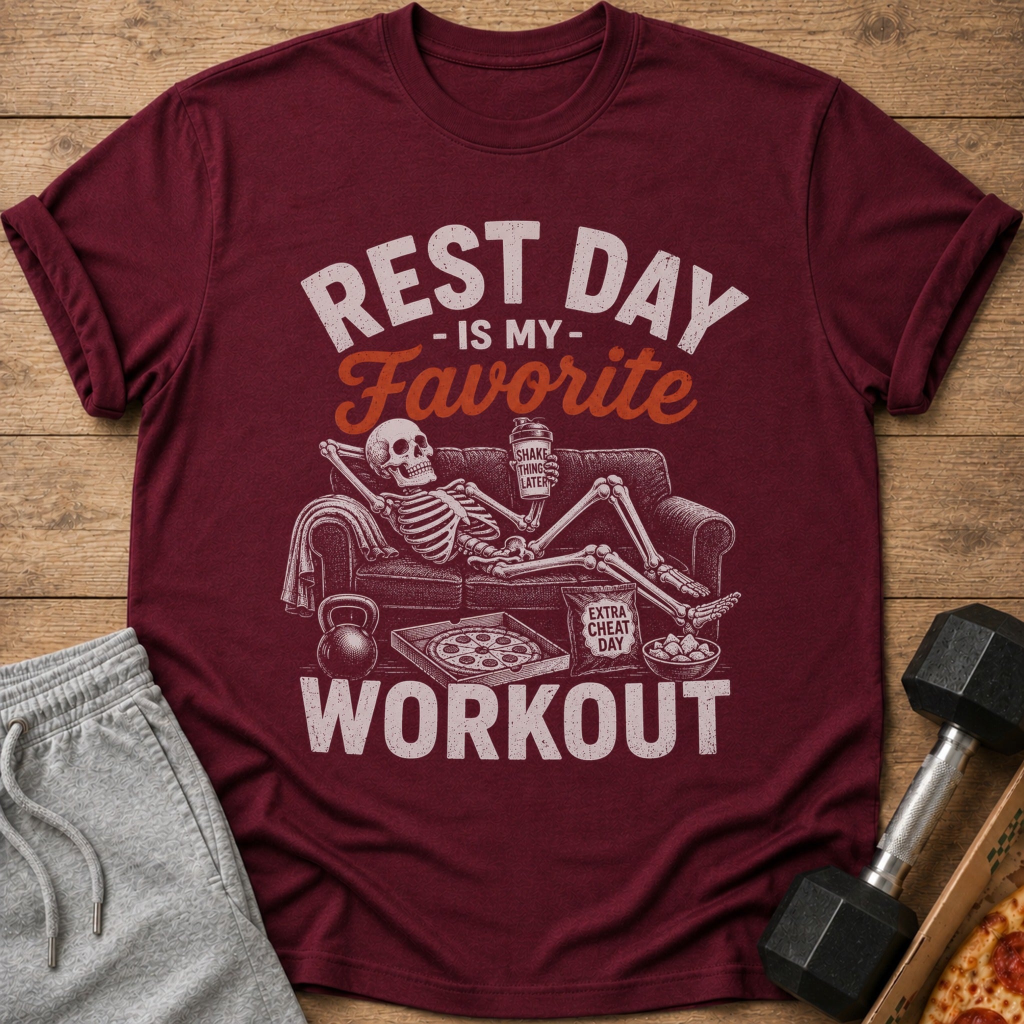 Maroon t-shirt with graphic: skeleton on couch, pizza, and text "Rest Day Is My Favorite Workout".