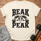 Cream t-shirt with black distressed text "BEAK PEAK" and a pelican lifting a barbell.