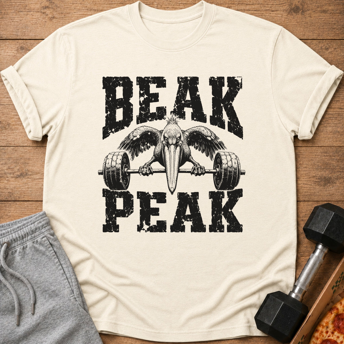 Cream t-shirt with black distressed text "BEAK PEAK" and a pelican lifting a barbell.