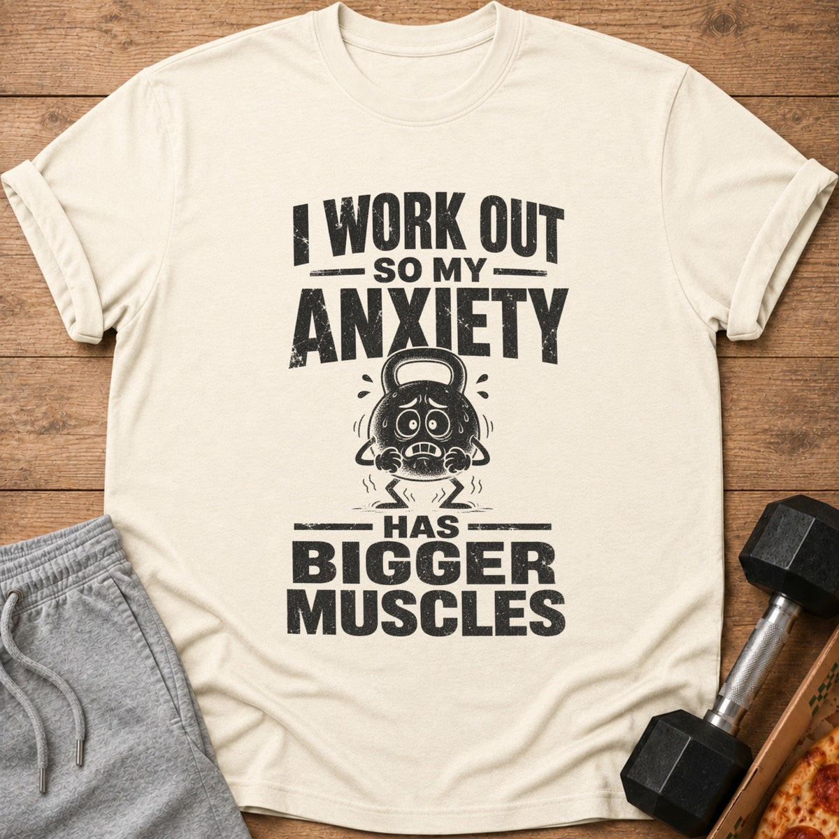 Cream t-shirt with text "I work out so my anxiety has bigger muscles" and a distressed kettlebell graphic.