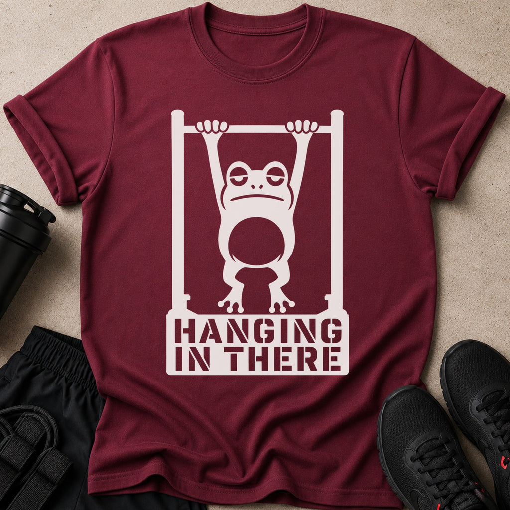Maroon t-shirt with distressed white graphic of frog hanging from bar and text "HANGING IN THERE".