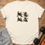 Cream t-shirt with a graphic of four black cats in autumn settings.