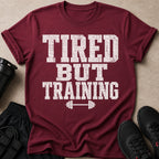 Maroon t-shirt with distressed white text that reads "TIRED BUT TRAINING" and a barbell graphic.