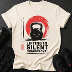 Cream t-shirt with a distressed kettlebell graphic and text "LIFTING IN SILENT DISAPPROVAL".