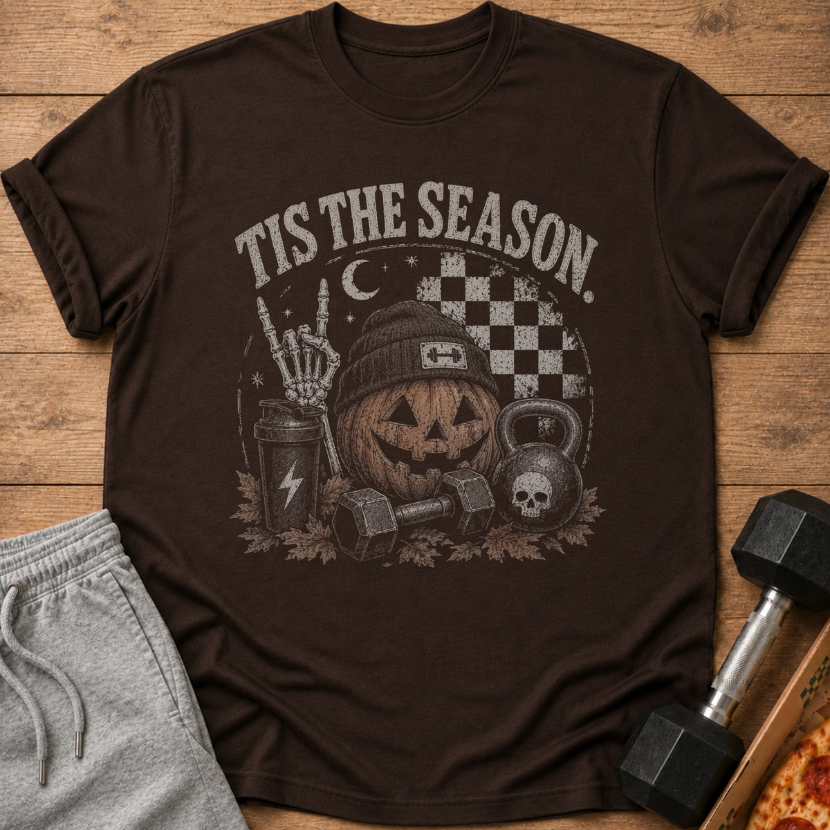 Brown t-shirt with "Tis The Season" text, pumpkin, skeleton hand, and workout equipment.