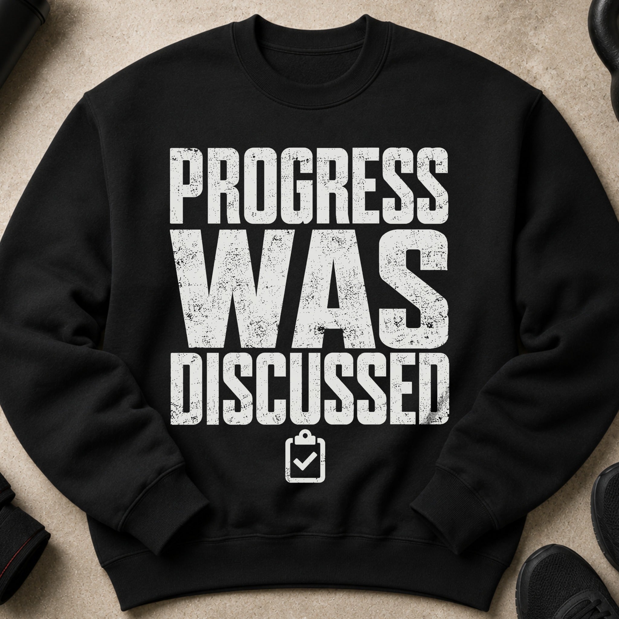 Black crewneck sweatshirt with white text "PROGRESS WAS DISCUSSED" and a clipboard icon.