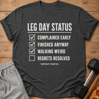 Dark grey t-shirt with "Leg Day Status" and a checklist: complained, finished anyway, walking weird, regrets resolved.