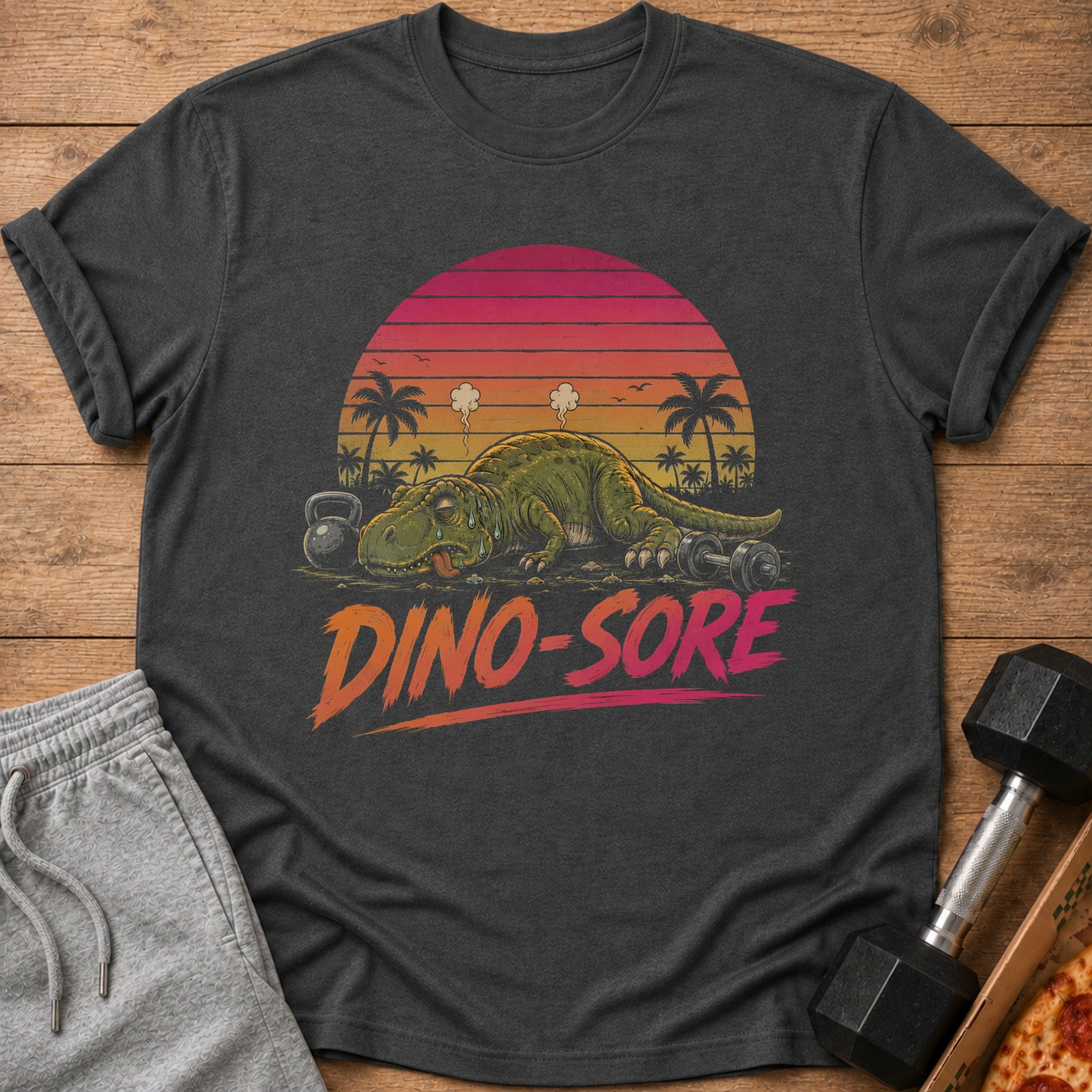 T-shirt with a tired dinosaur next to weights and dumbbells, text says "DINO-SORE".