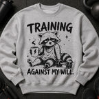 Grey crewneck sweatshirt with cartoon raccoon holding coffee, text "TRAINING AGAINST MY WILL."